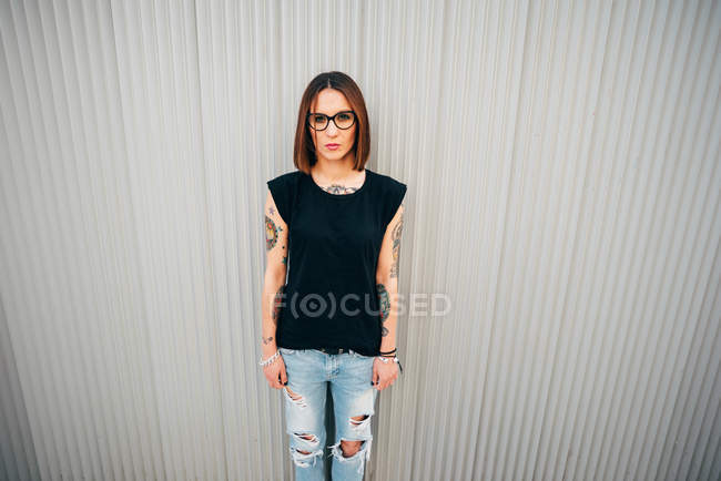 Стильна молода жінка стоїть на металевій стіні і дивиться на камеру — стокове фото