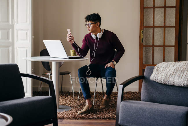 Hombre joven sentado junto a la computadora portátil y el reproductor de medios de navegación en casa - foto de stock