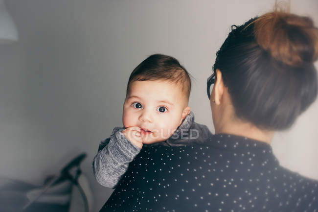 Adorable boy looking at camera while sitting on mother hands — Stock Photo