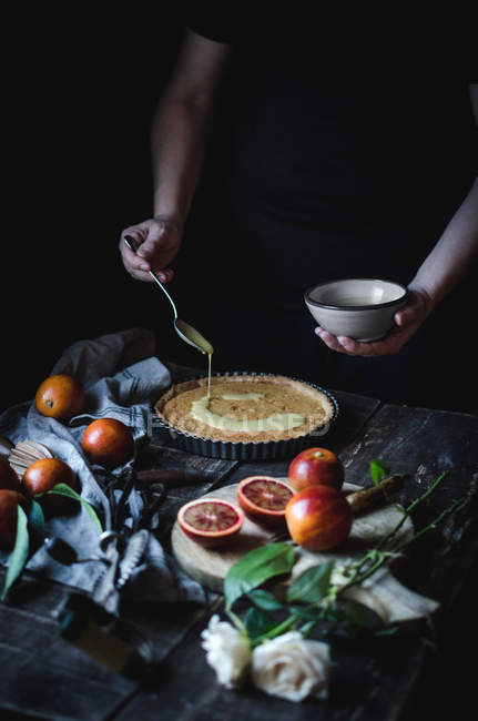 Crop unrecognizable cook putting custard on tart on rustic table. — Stock Photo