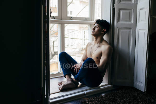 Pensativo homem sem camisa posando na soleira da janela — Fotografia de Stock