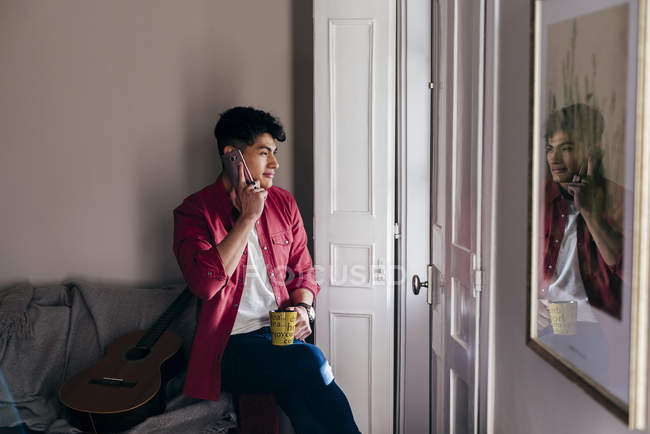 Uomo allegro con telefono e tazza a casa — Foto stock