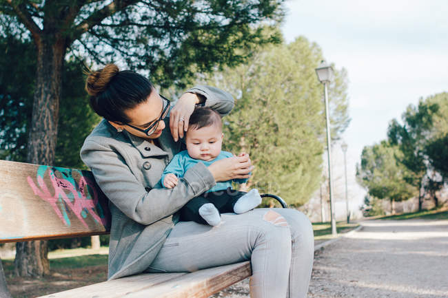 Веселая женщина с ребенком на руках на скамейке в парке — стоковое фото