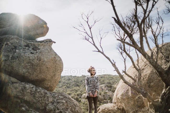 Jovem mulher de pé perto de penhascos e árvores nuas — Fotografia de Stock
