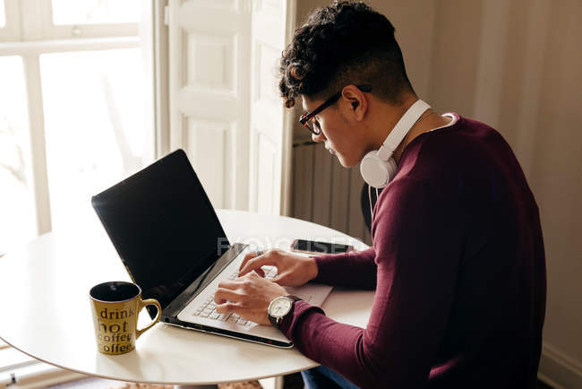 Молодий чоловік сидить за столом і друкує на ноутбуці вдома . — стокове фото