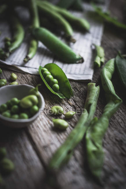 Close up view of green peas and newspaper on wooden table — Stock Photo