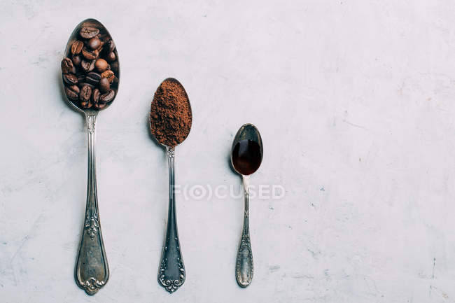 Row of spoons with coffee beans, ground coffee on wihite background — Stock Photo