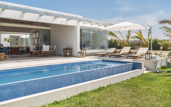 Großer blauer Pool und bequeme Liegestühle unter Sonnenschirm auf Villa an sonnigen Tagen. — Stockfoto