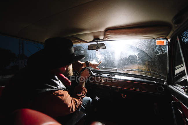 Homme barbu dans le chapeau voiture de conduite et pointant avec la main devant — Photo de stock