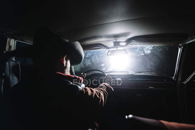 Вид сзади человека в шляпе за рулем автомобиля в ночное время — стоковое фото