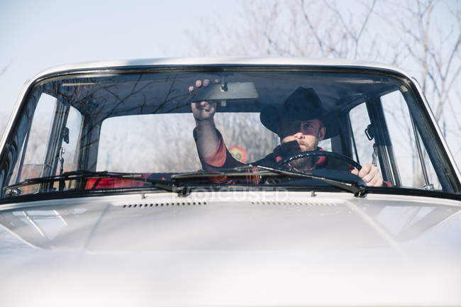 Человек в шляпе регулирует зеркало заднего вида автомобиля — стоковое фото