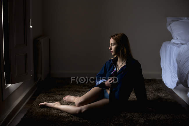 Seitenansicht einer gelassenen Frau, die auf dem Boden im Zimmer posiert — Stockfoto