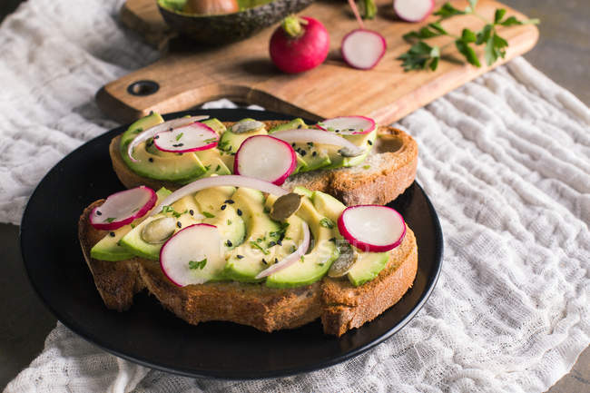 Натюрморт тостів з авокадо та шматочками редьки на тарілці — стокове фото
