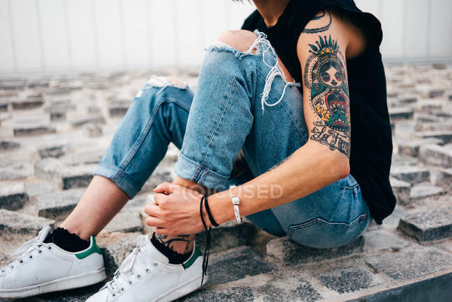 Cropped image of woman with colorful tattoos sitting on pavement on street. — Stock Photo