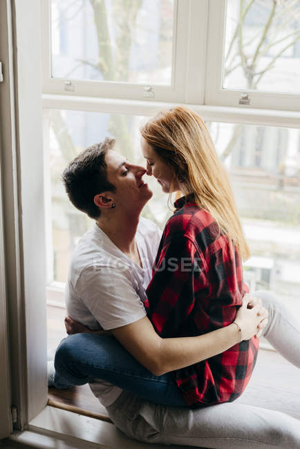 Junges Paar umarmt sich auf Fensterbank — Stockfoto