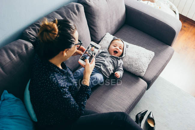 Усміхнена жінка робить знімки маленького сина, що лежить на тренері — стокове фото