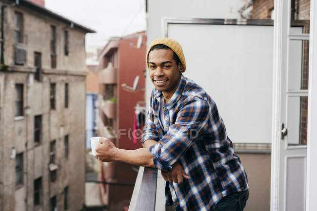 Smiling man posing with coffee on balcony — Stock Photo