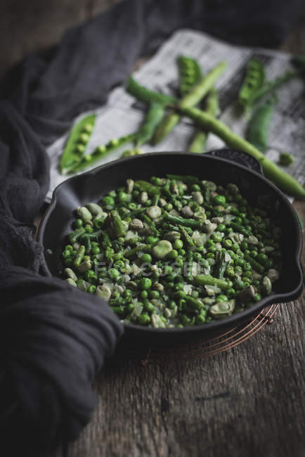 Bodegón de sartén lleno de guisantes verdes sobre mesa rústica - foto de stock