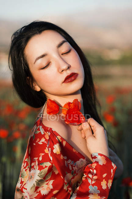 Morena con los ojos cerrados posando con flores de amapola - foto de stock
