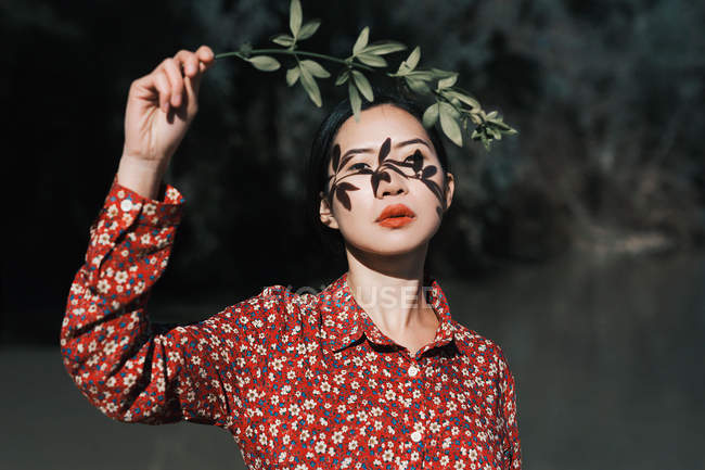 Young woman posing with branch throwing shadow on face — Stock Photo