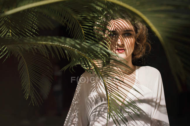 Jovem mulher de vestido branco posando na folha de palma e olhando para a câmera — Fotografia de Stock