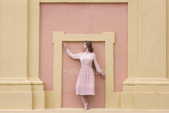 Pretty young woman in pink dress posing at pink facade — Stock Photo