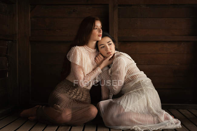 Young brunette girls sitting in tender embrace on wooden floor of cabin — Stock Photo