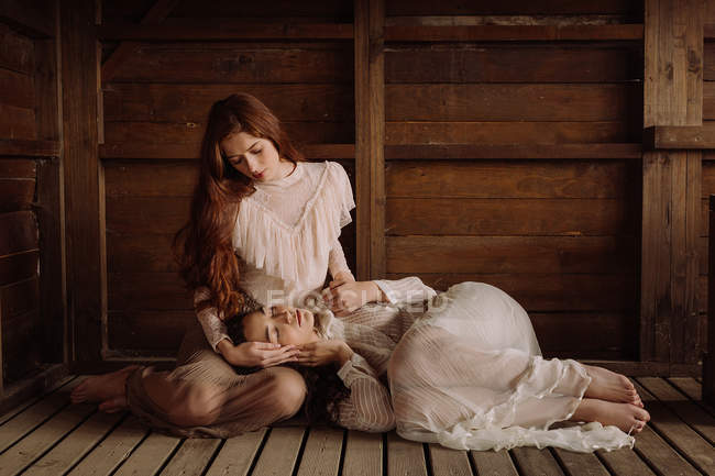 Young brunettes sitting in tender embrace on wooden floor of cabin — Stock Photo