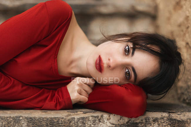 Брюнетка в красном платье лежит на каменной ступеньке и смотрит в камеру . — стоковое фото