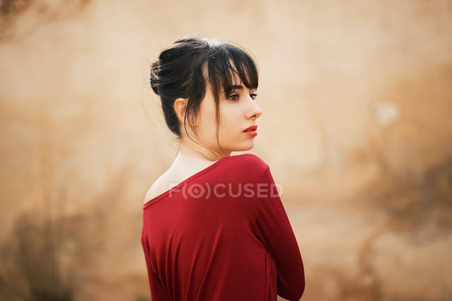 Chica seductora en vestido rojo mirando por encima del hombro de distancia - foto de stock