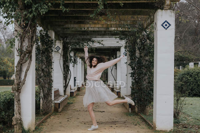 Щаслива жінка стрибає в алеї з зеленими повзаючими рослинами на білих колонах — стокове фото
