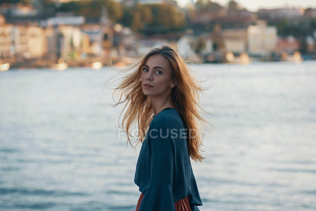 Frau blickt gegen Küstenstadt über die Schulter in Kamera — Stockfoto