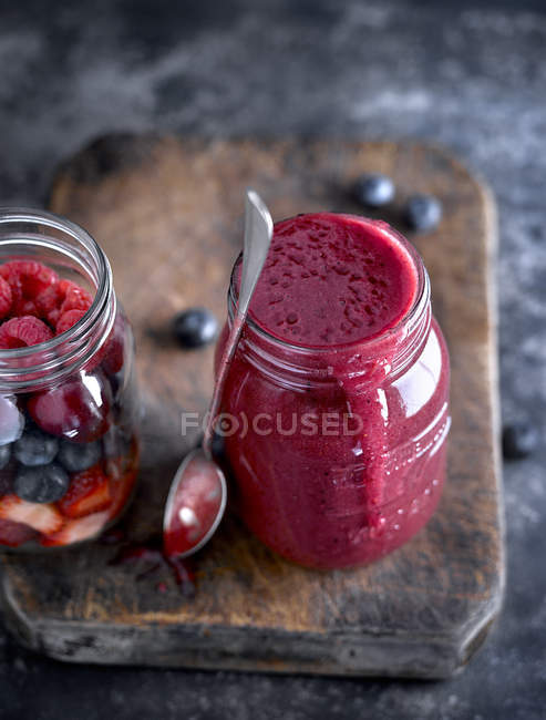 Close-up of glass jar filled with red smoothie and spoon on wooden board. — Stock Photo