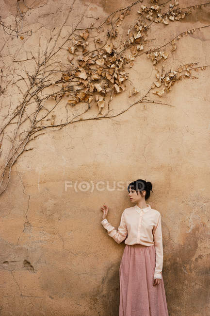 Frau steht an Wand mit trockenem Laub — Stockfoto