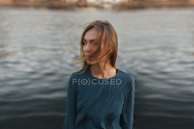 Femme sereine posant contre l'eau et détournant les yeux — Photo de stock
