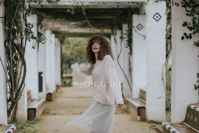 Мрійлива жінка позує в красивій алеї з білими колонами — стокове фото