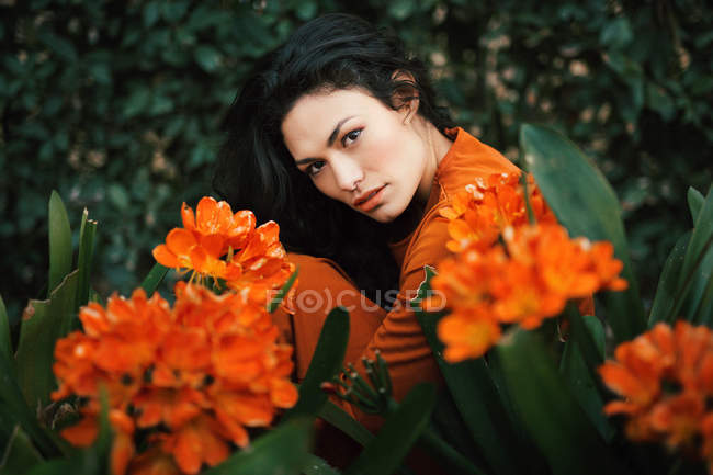 Молода жінка позує в яскраво-помаранчевих квітах, дивлячись на камеру — стокове фото