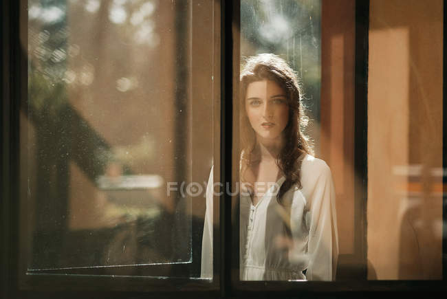Woman in white dress posing behind glass in doorway — Stock Photo