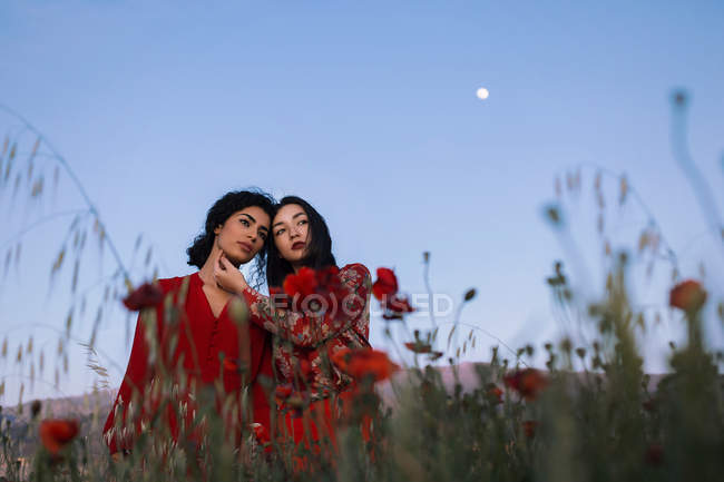 Молодые женщины, стоящие в зеленой траве нежно касаясь лица и глядя в сторону . — стоковое фото