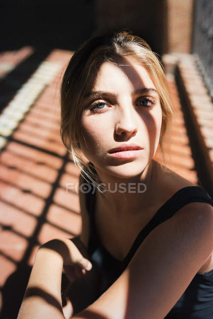 Jeune fille blonde regardant sans émotion la caméra sous les rayons du soleil . — Photo de stock