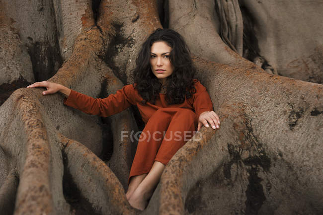 Attraktive brünette Frau sitzt in großen Baumwurzeln. — Stockfoto