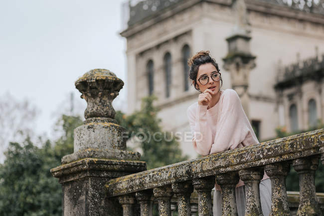 Young girl in glasses leaning on old stone handrail of beautiful castle and looking away. — Stock Photo