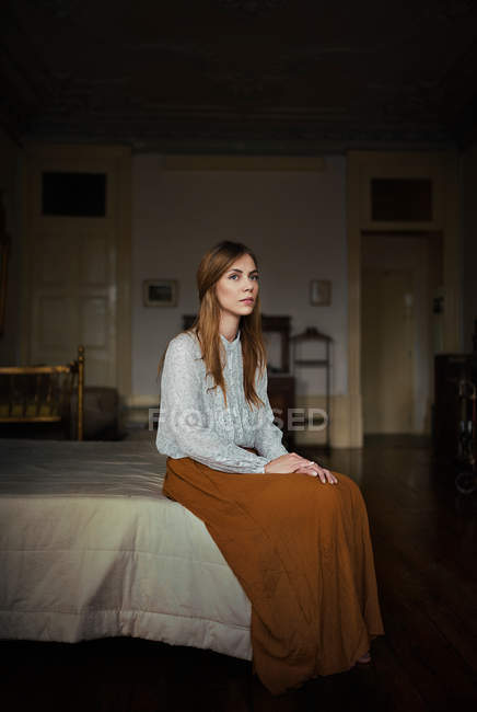 Pensive young woman sitting ob bed in apartment — Stock Photo