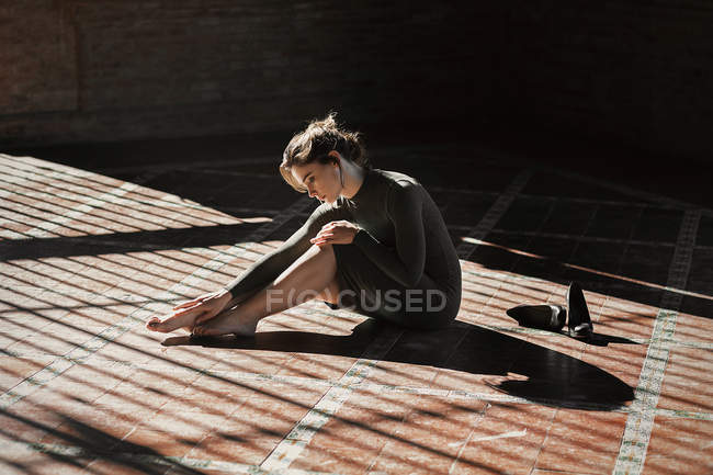Брюнетка, сидящая на полу в солнечных лучах и касаясь ног — стоковое фото