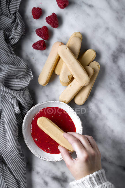 Обрезать женскую руку, макая печенье в малиновый джем — стоковое фото