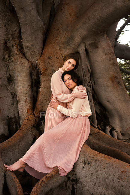 Hübsche Frauen in Vintage-Kleidern umarmen sich am riesigen Baum. — Stockfoto