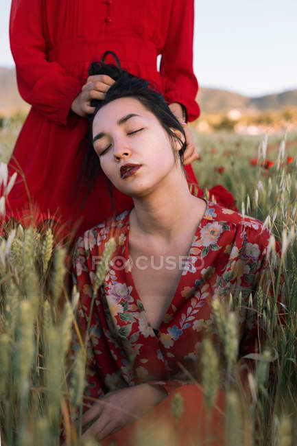 Faceless woman in red holding hair of brunet tenderly with eyes closed in country field — Stock Photo