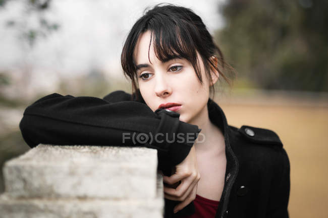 Melancholic woman in black leaning on fence — Stock Photo