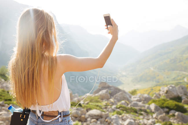 Menina loira fazendo selfie no vale ensolarado em montanhas — Fotografia de Stock
