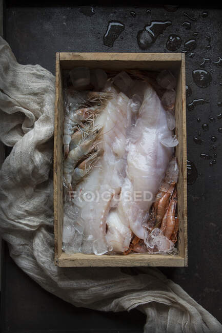 También vista de pescado crudo y diferentes mariscos en hielo en caja de madera. - foto de stock